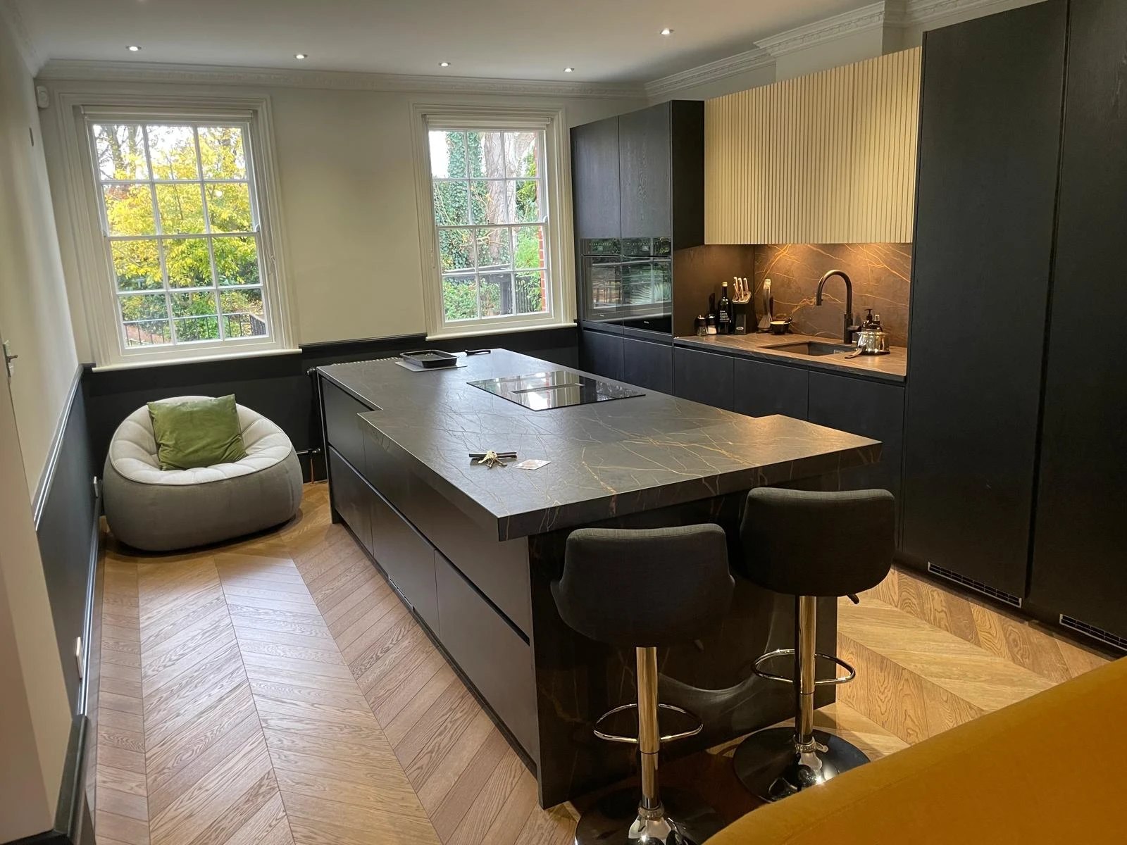 Black oak handleless kitchen with a stone island and breakfast bar on a chevron oak floor