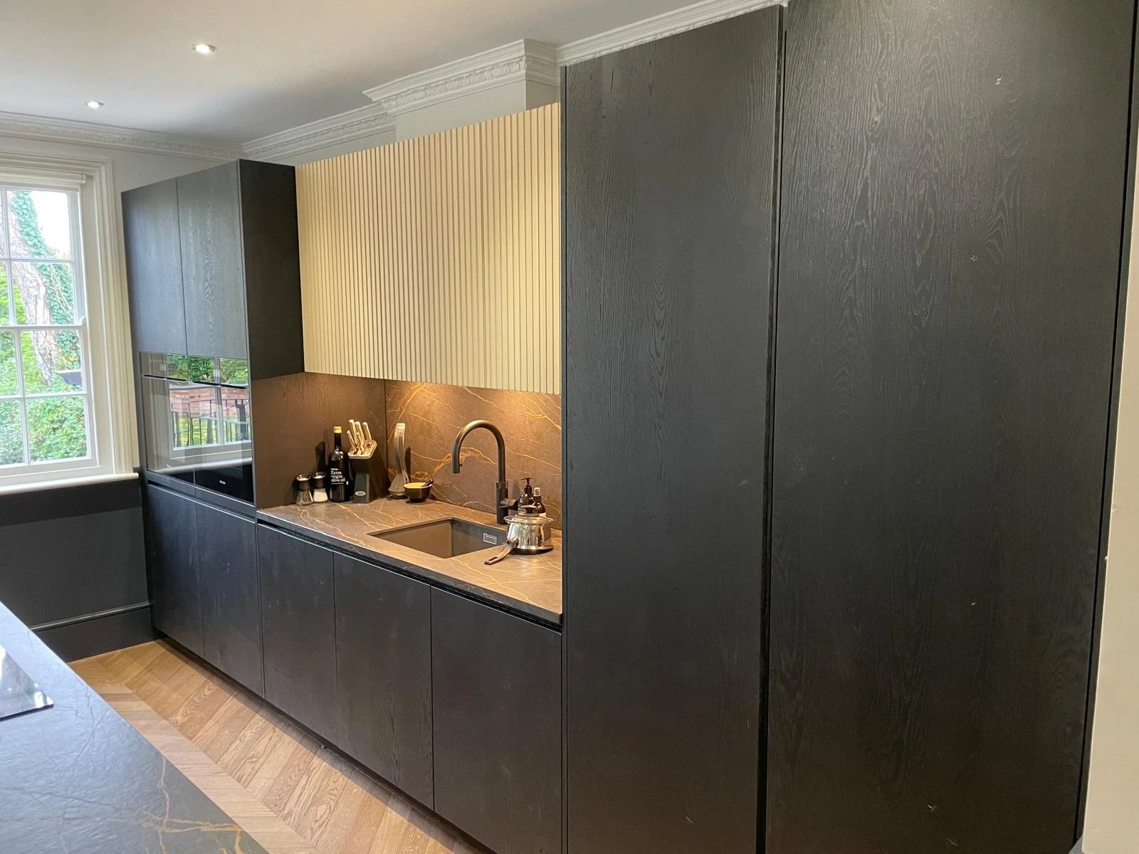 Black oak kitchen run with fluted wall units over a stone splashback