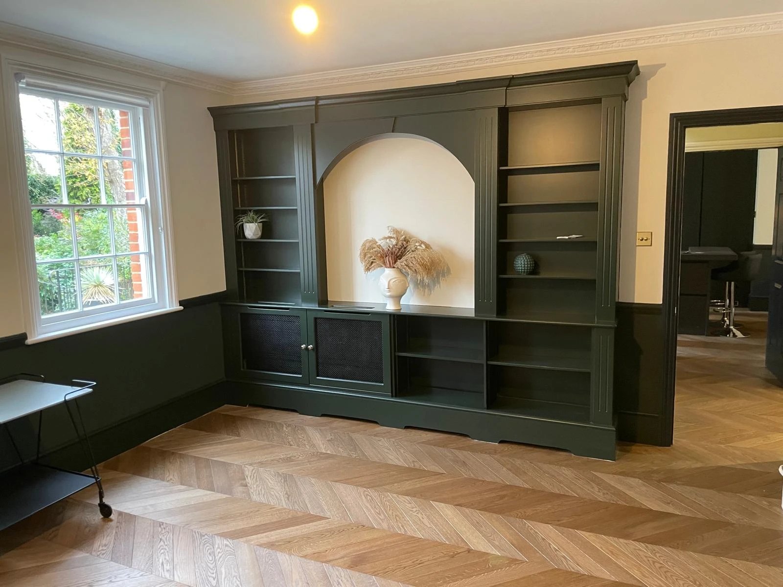 Deep green bespoke bookcase wall with an arched niche and radiator covers
