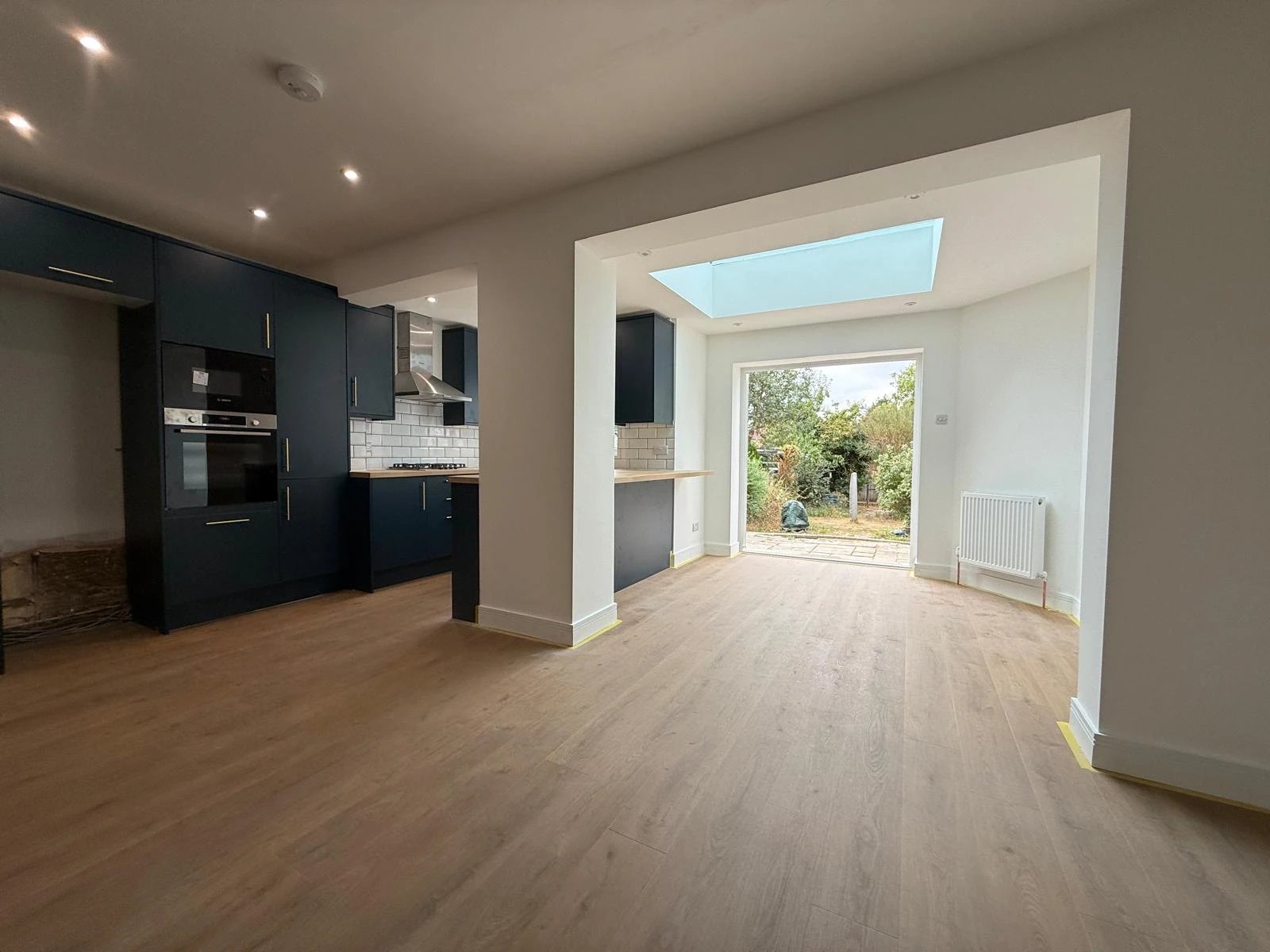 Rear extension with a roof lantern opened up to a navy kitchen, with one oak effect floor running through