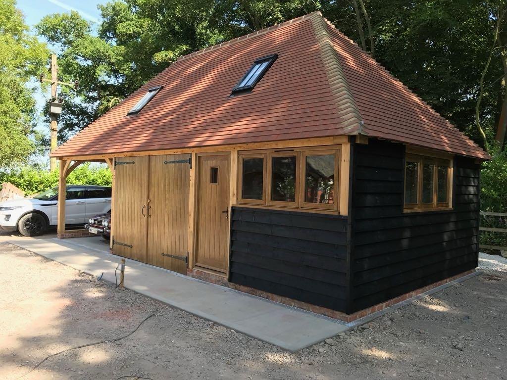 Oak framed garage with black weatherboarding and a hipped clay tile roof