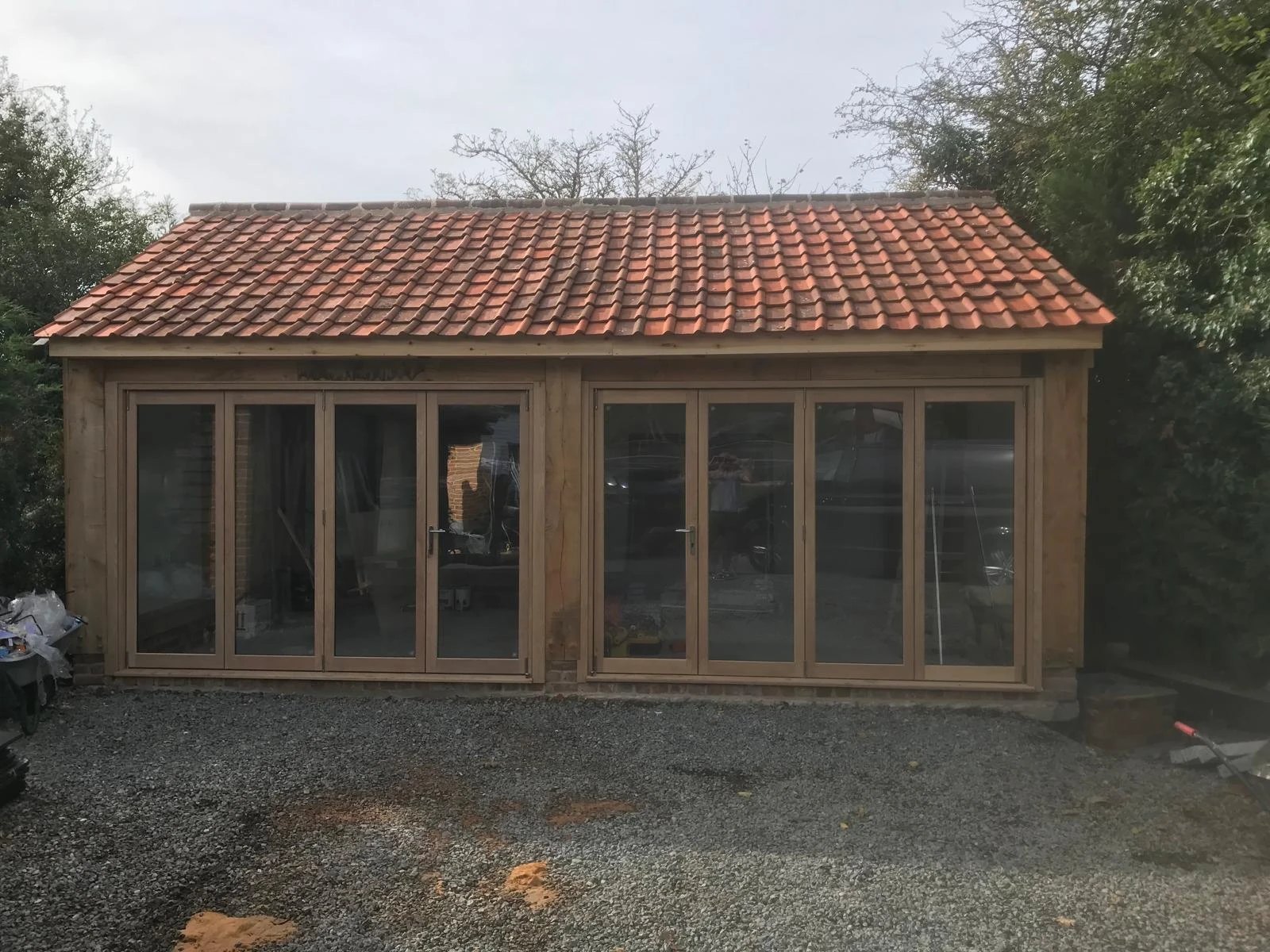 Oak framed garden building with two sets of folding glazed doors and a clay tile roof