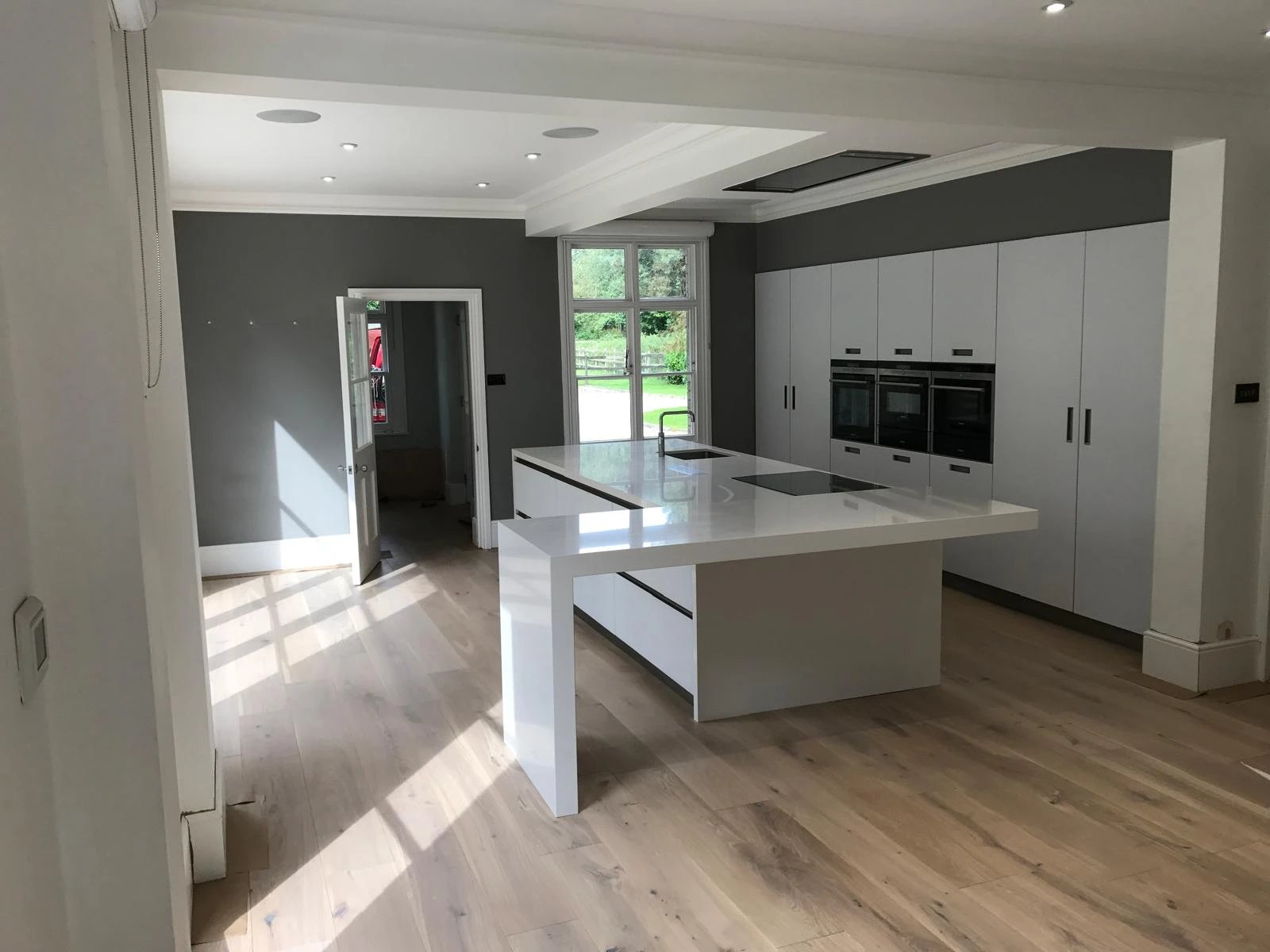 Open plan white kitchen with a quartz island and wide oak boards
